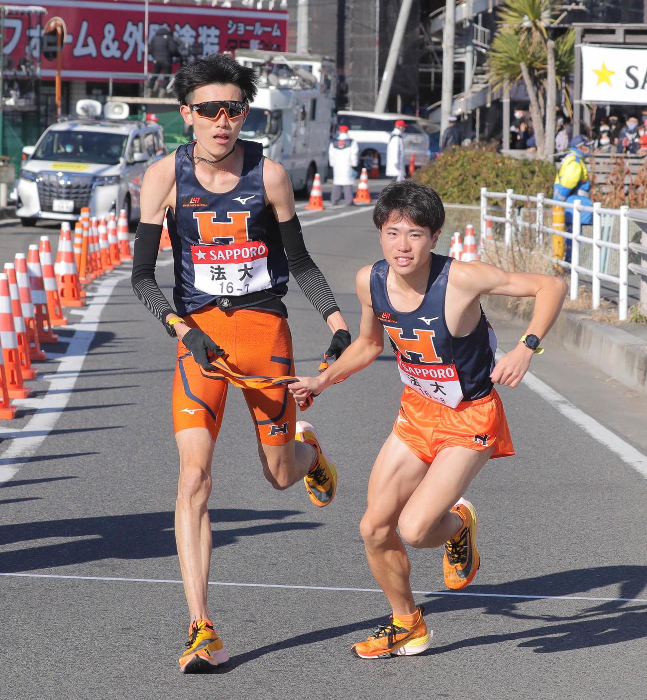 平塚中継所でタスキをつなぐ法大7区の中園（左）のと8区の稲毛（代表撮影）