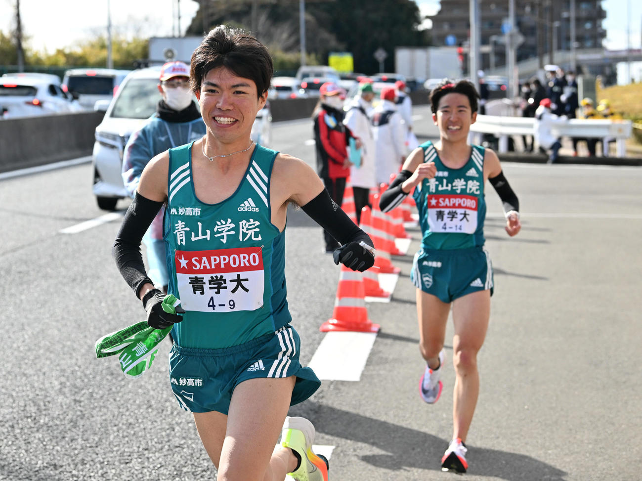 戸塚中継所で青学大8区佐藤（奥）からたすきを受け笑顔で走り出す9区中村（撮影・滝沢徹郎）