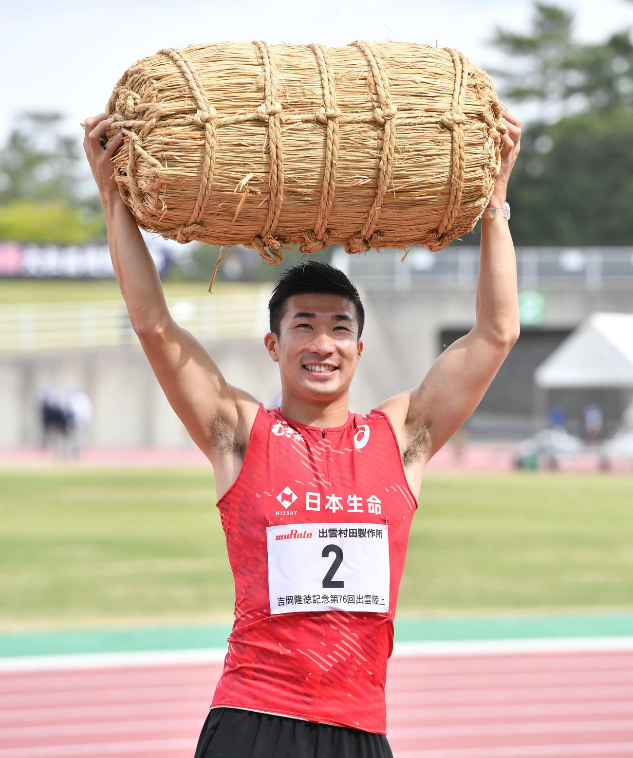 YOSHIOKAスプリント男子100メートルで優勝した桐生は、副賞で贈られた米俵を笑顔で抱える（撮影・岩下翔太）