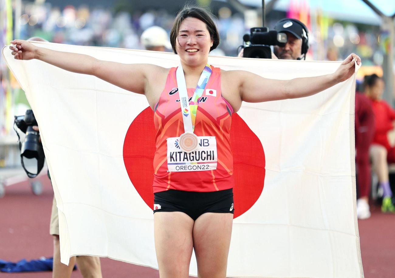 陸上世界選手権の女子やり投げで銅メダルを獲得し、日の丸を背に笑顔の北口榛花（代表撮影）