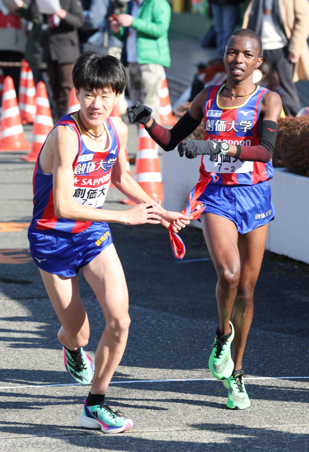戸塚中継所で創価大2区ムルワ（右）は3区山森にたすきを渡す（撮影・宮地輝）