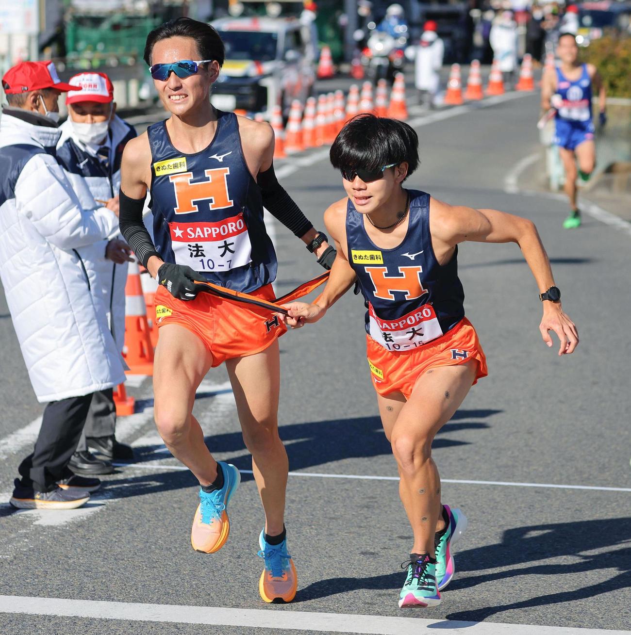 平塚中継所で7区の宮岡幸大（左）からたすきを受け取り、走り出す法大8区の宗像直輝（代表撮影）（共同）