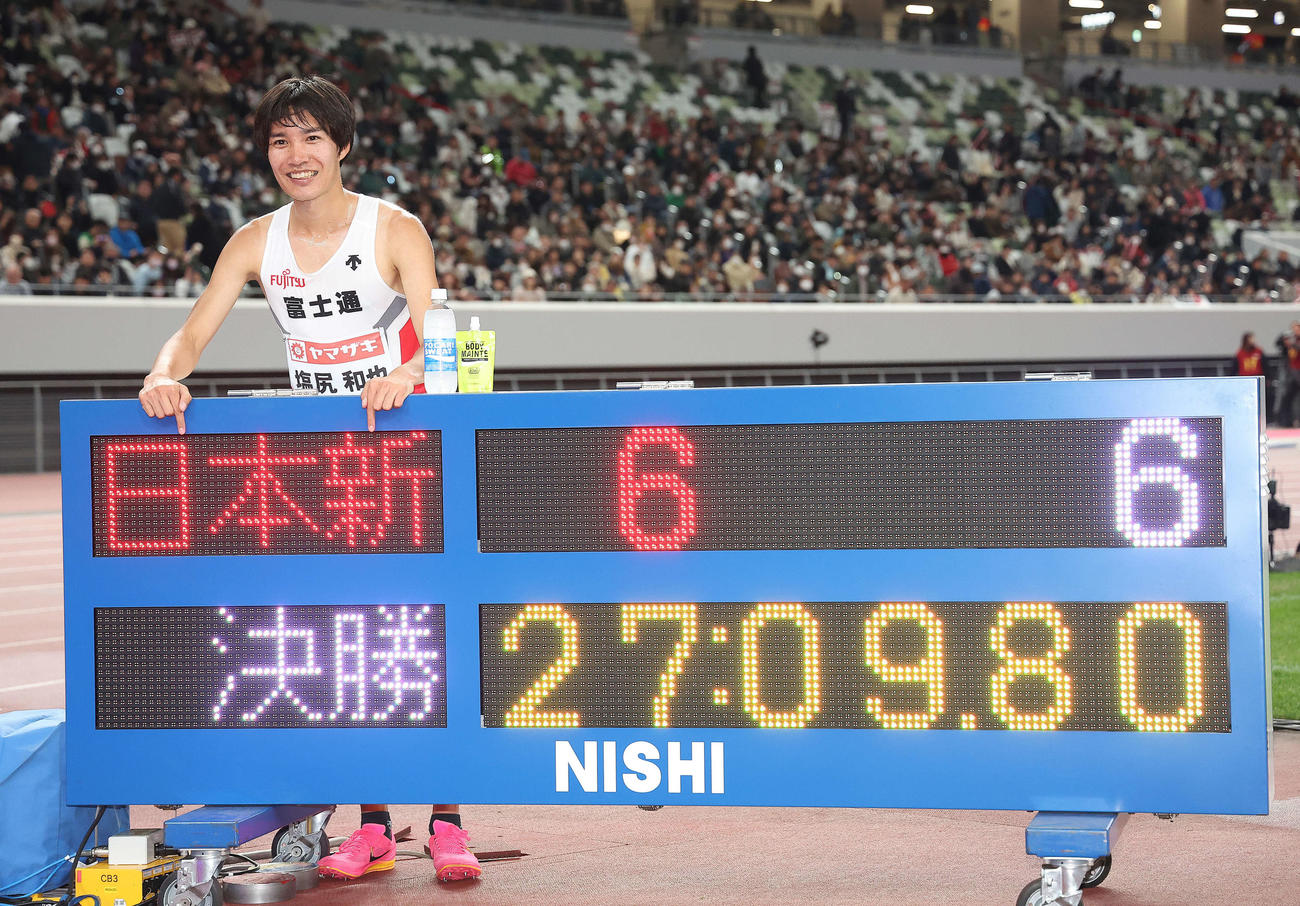 男子1万メートル　日本新記録で優勝を果たし、27分9秒80が表示された電光掲示板を指さす塩尻（撮影・河田真司）