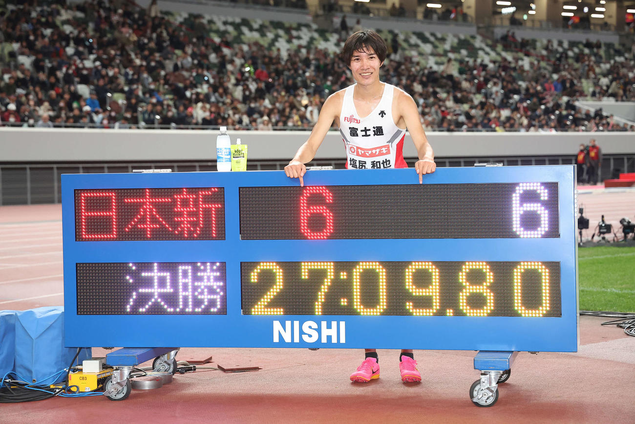 男子1万メートル　日本新記録で優勝を果たし、27分9秒80が表示された電光掲示板を指さす塩尻（撮影・河田真司）