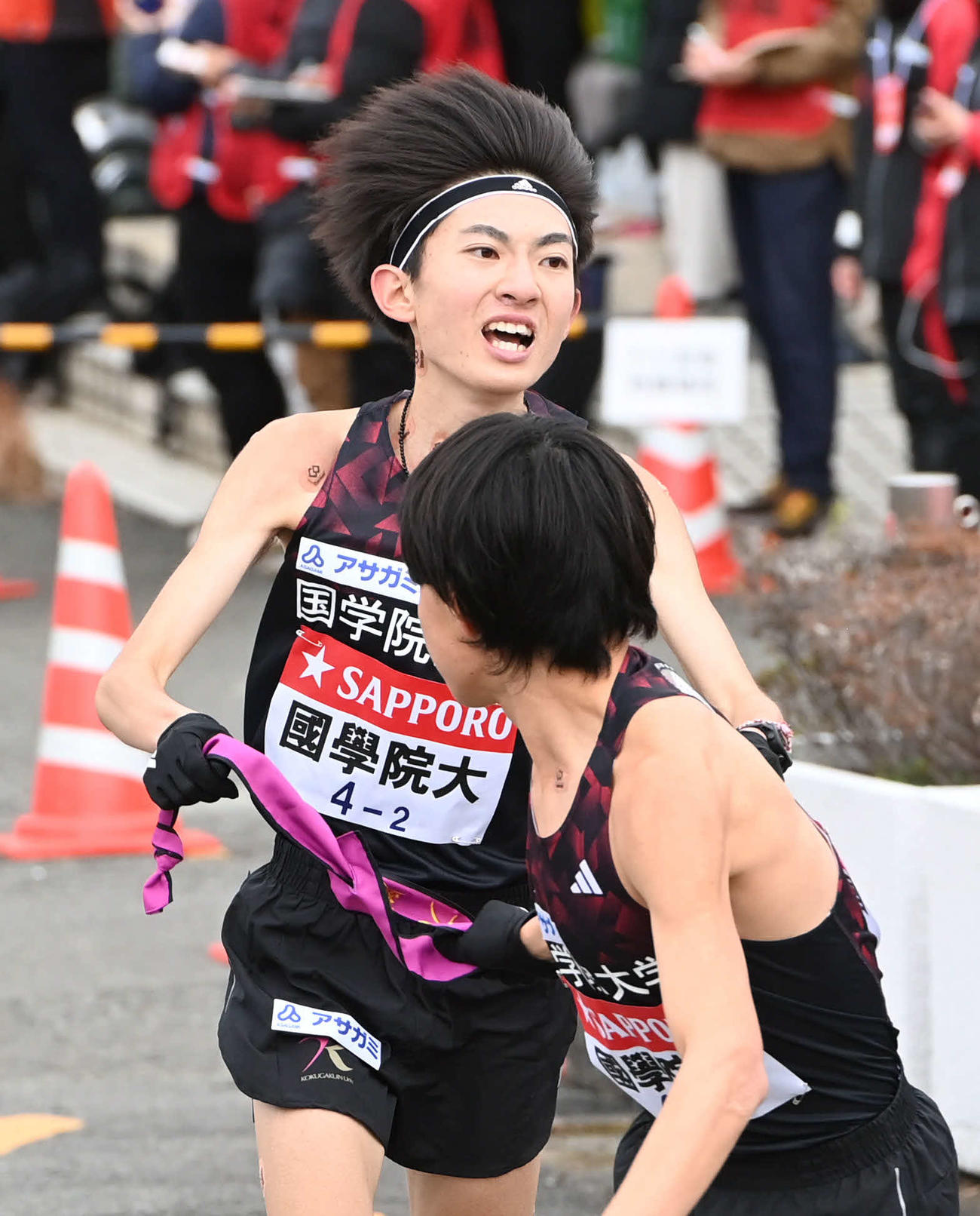 国学院大2区平林（後方）は3区青木にたすきを渡す（撮影・山崎安昭）