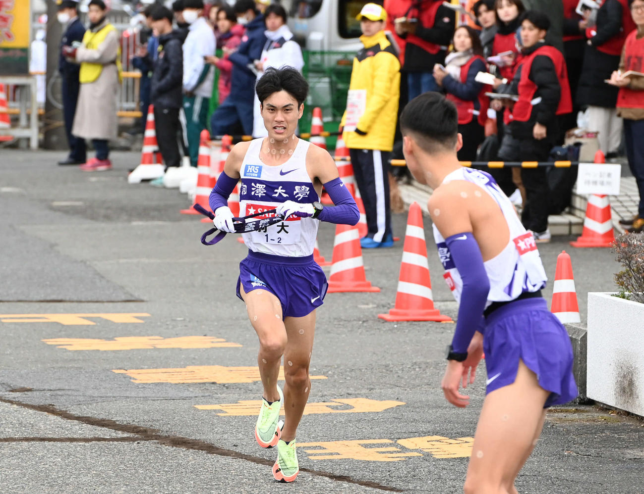 戸塚中継所にトップで駆け込む駒大2区鈴木。手前は3区佐藤（撮影・山崎安昭）