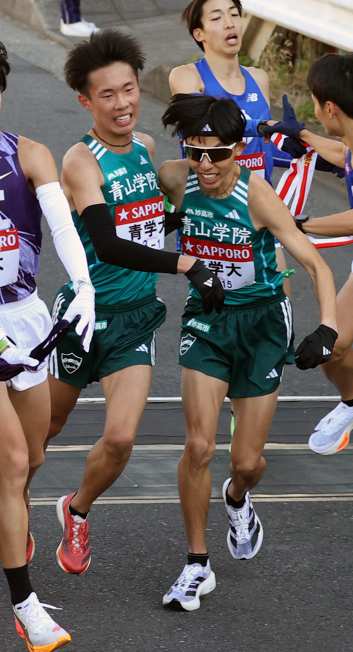 青学大1区荒巻（左）は2区黒田にたすきを渡す（撮影・大野祥一）