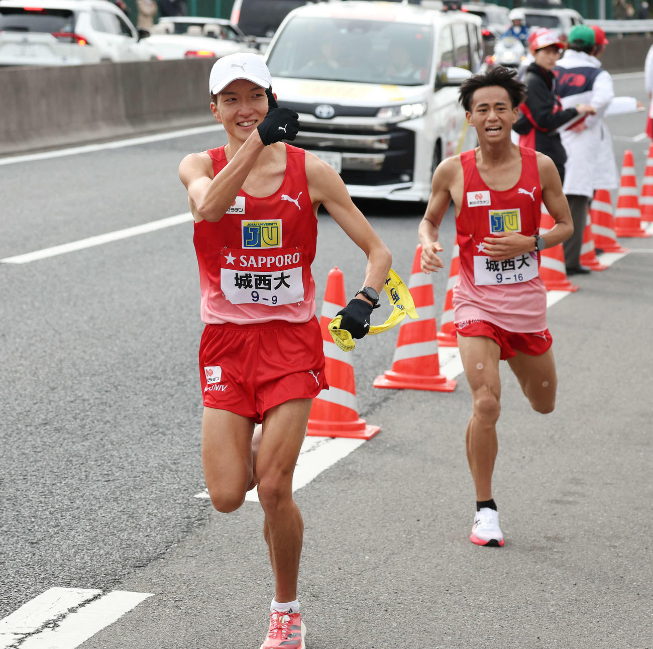 戸塚中継所で城西大8区小田（右）からタスキを受け取り、サムズアップして駆け出す9区平林（撮影・宮地輝）
