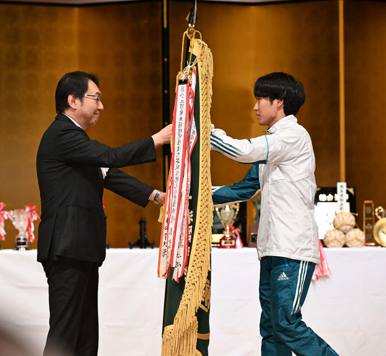 総合優勝を決め、読売新聞東京本社の村岡社長（左）から優勝旗を受け取る青学大の佐藤（代表撮影）