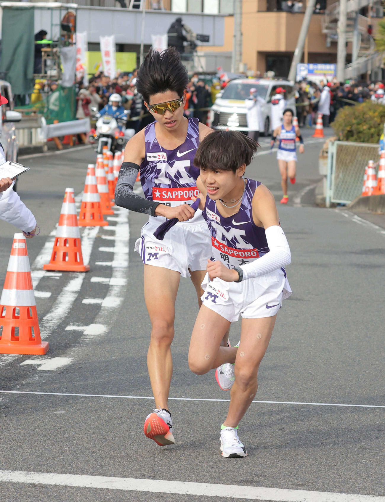 平塚中継所でタスキをつなぐ明大7区の尾崎（左）と明大8区の綾（代表撮影）