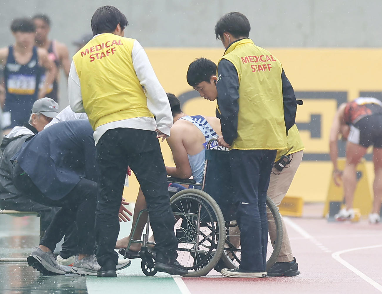 男子100メートル予選1組　スタート直後に足を痛め途中棄権となり、車椅子で運ばれる多田（中央）（撮影・前田充）