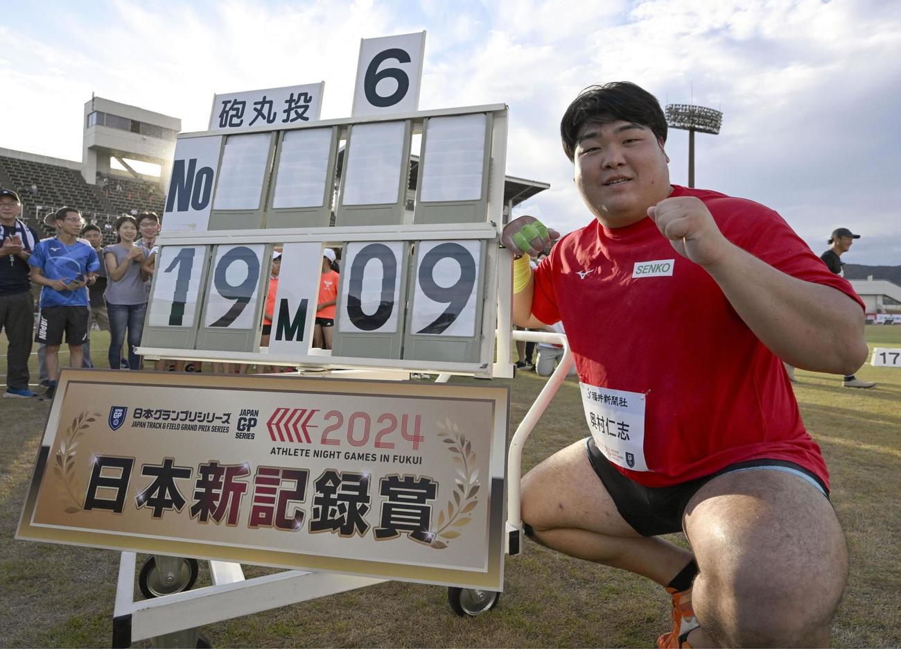 男子砲丸投げを19メートル09の日本新で制し、記録掲示板の前でポーズをとる奥村（共同）