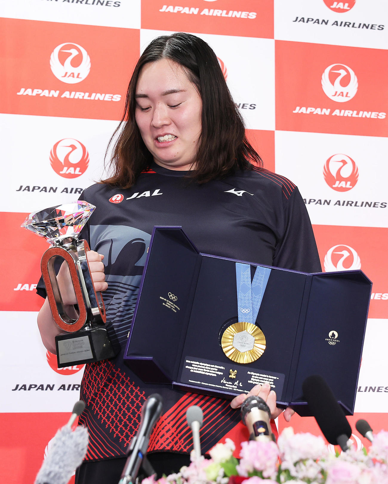 パリ五輪金メダルとダイヤモンドリーグのトロフィーを重たそうにおどけながら持ち上げる北口（撮影・足立雅史）