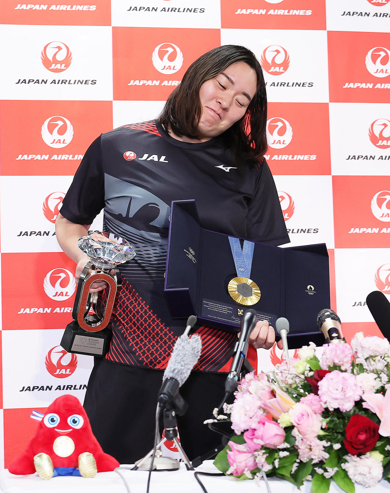 パリ五輪金メダルとダイヤモンドリーグのトロフィーを重たそうにおどけながら持ち上げる北口（撮影・足立雅史）