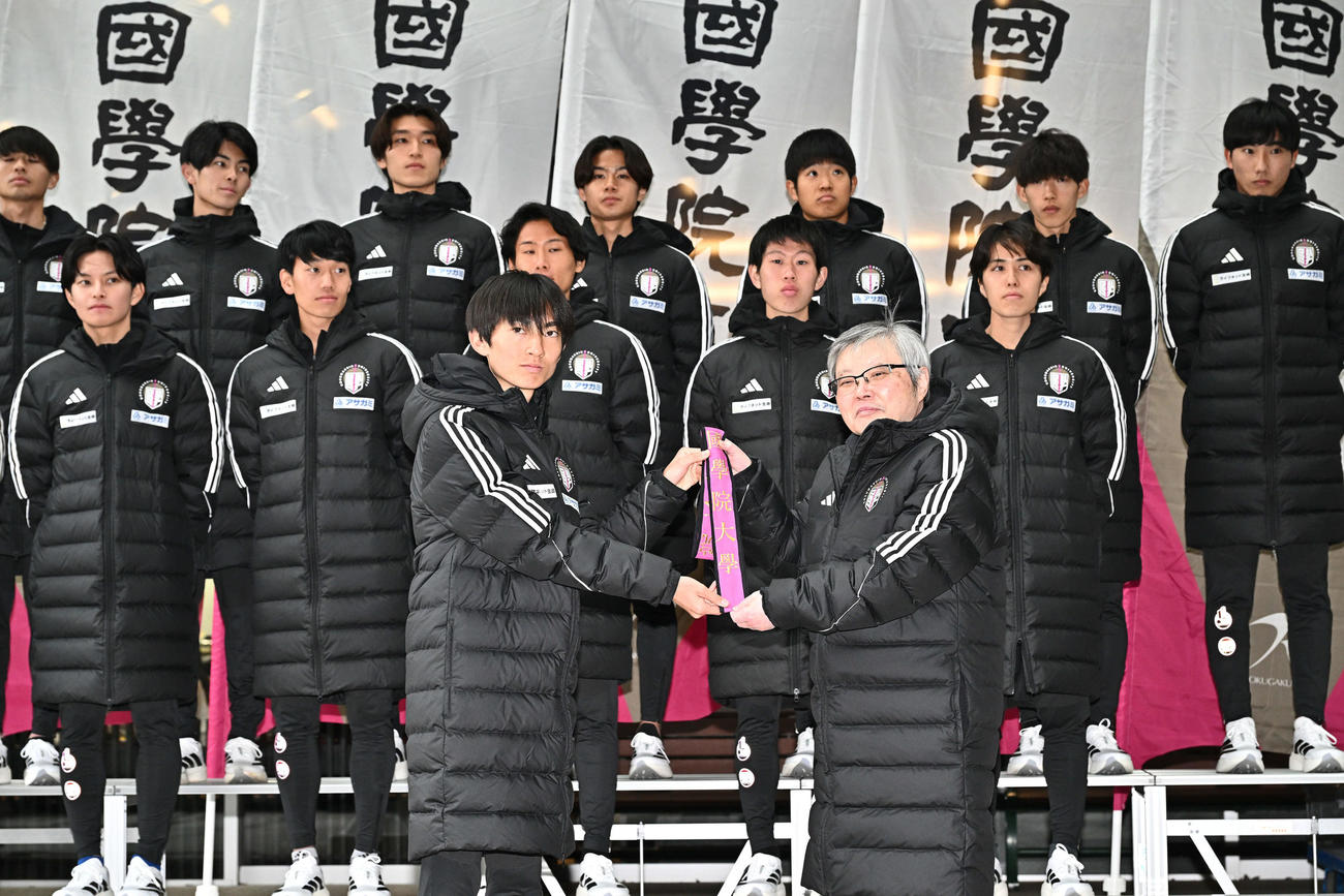 国学院大・針本正行学長（手前右）からたすきを受け取る平林（撮影・滝沢徹郎）