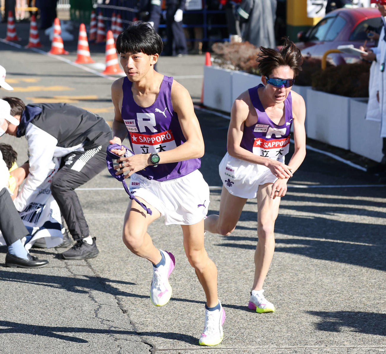 戸塚中継所で立教大3区稲塚（左）は2区馬場からタスキを受け駆け出す（撮影・宮地輝）