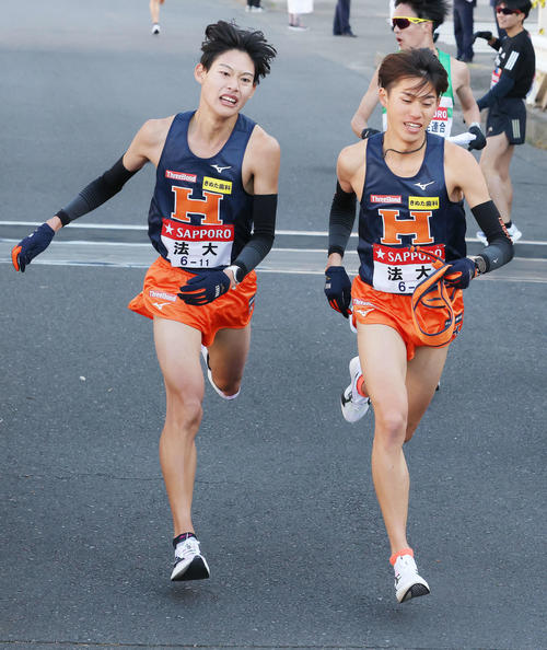 鶴見中継所を15位でタスキリレーする法大1区武田（左）と2区小泉（撮影・河田真司）