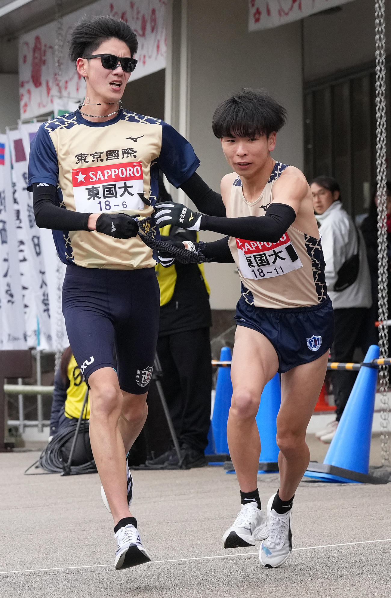 東京国際大6区中山（左）は7区冨永に小田原中継所でたすきを渡す（撮影・鈴木みどり）