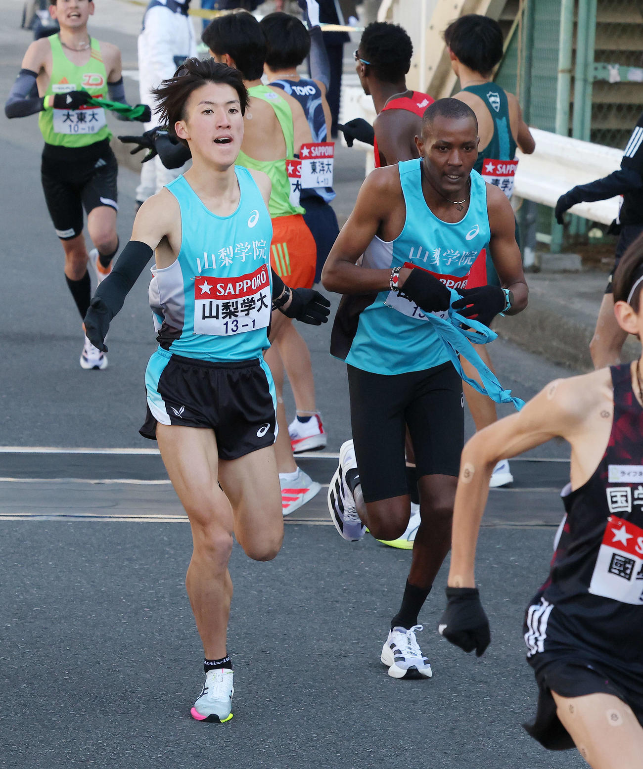 鶴見中継所を7位でタスキリレーする山梨学院大1区平八重（左）と2区ムトゥク（撮影・河田真司）