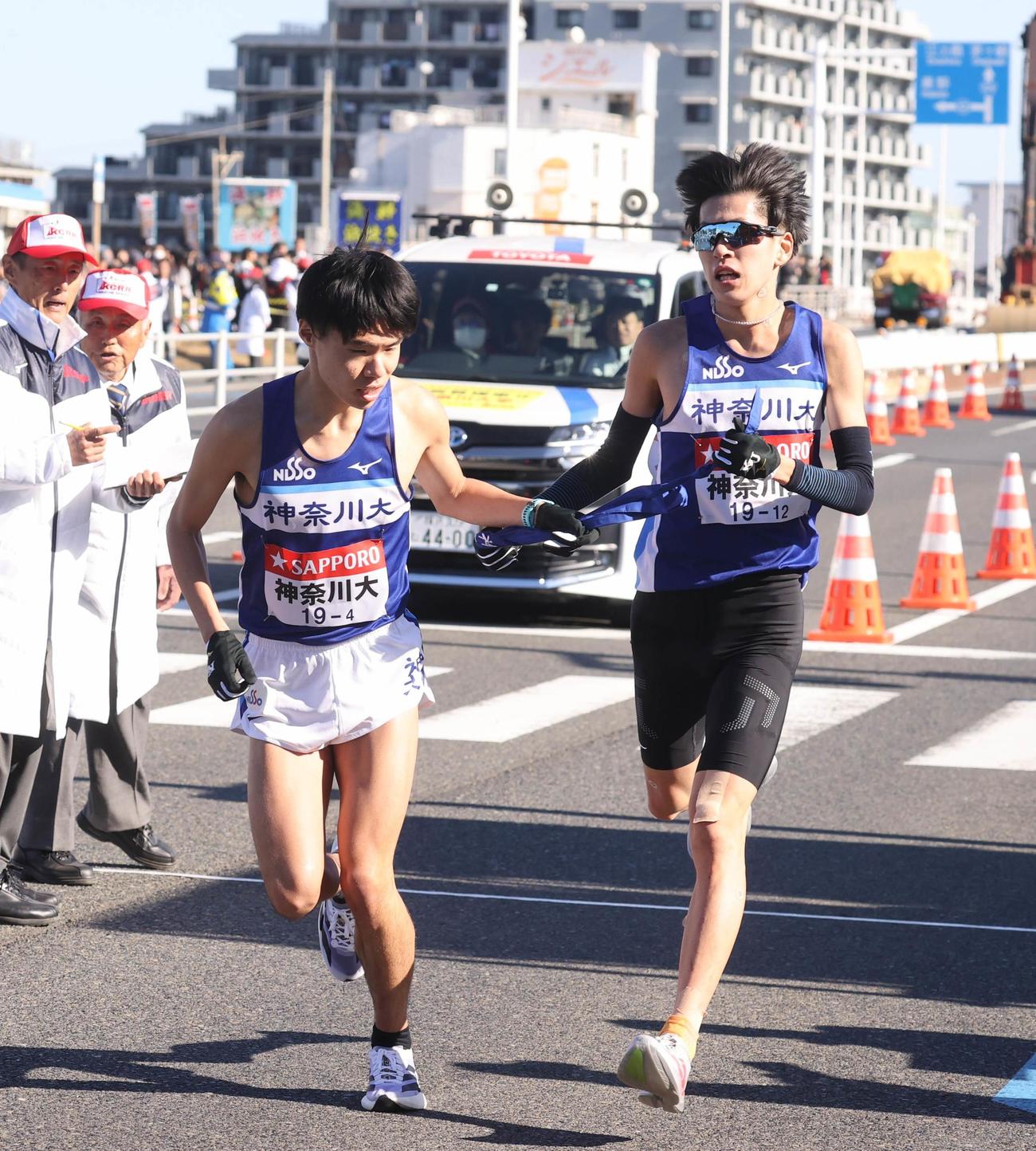 平塚中継所でタスキをつなぐ神奈川大3区の酒井健成（右）と4区の近藤大智（代表撮影）