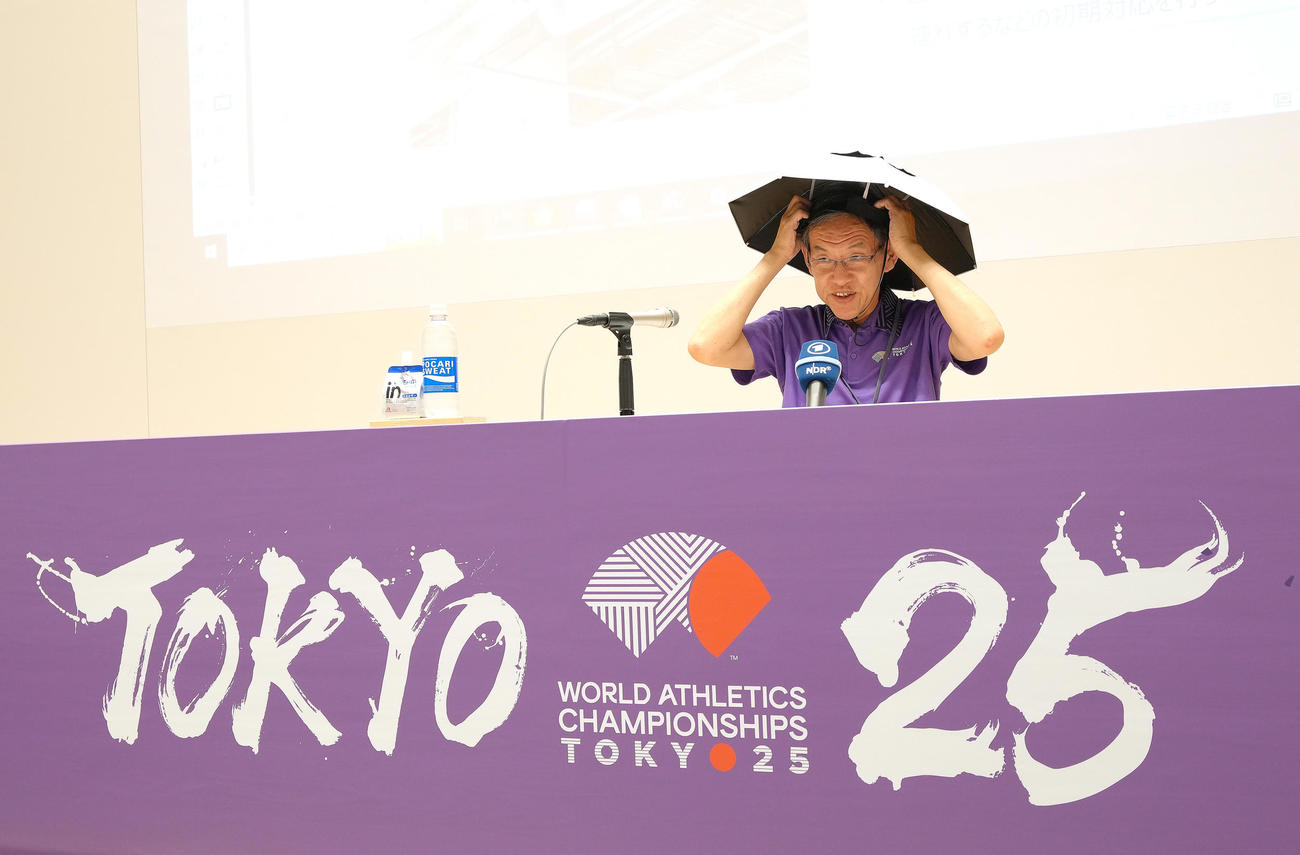 観客らに貸し出しするかさを頭につけ実演する東京2025世界陸上財団の武市事務総長（撮影・足立雅史）