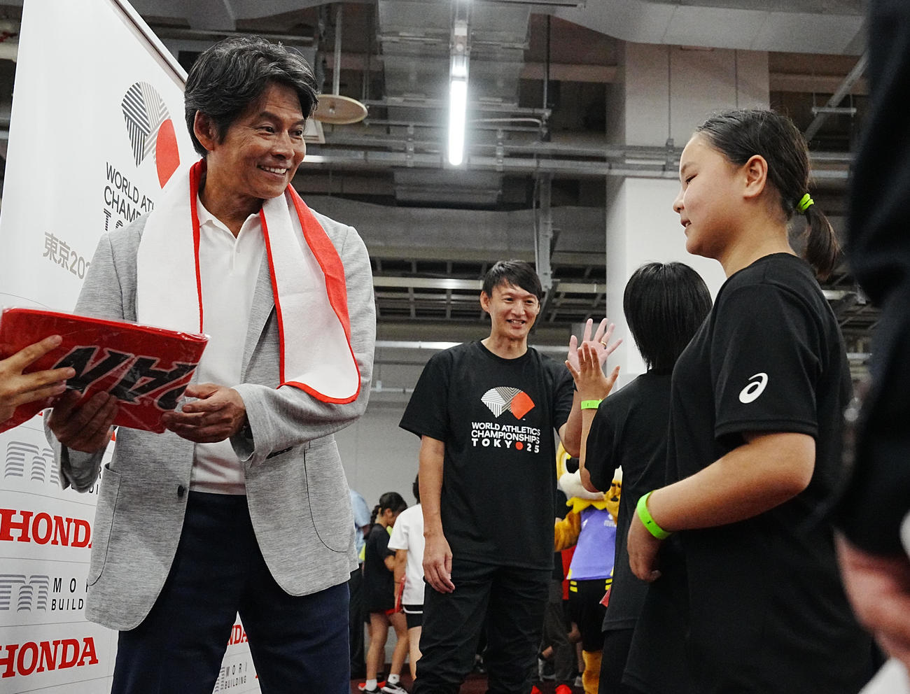 東京2025世界陸上「バトンプロジェクト」特別イベントで参加さした子どもたちにプレゼントを手渡す大会スペシャルアンバサダーの織田裕二。奥は北京五輪銀メダリストの高平慎士＝2025年9月5日