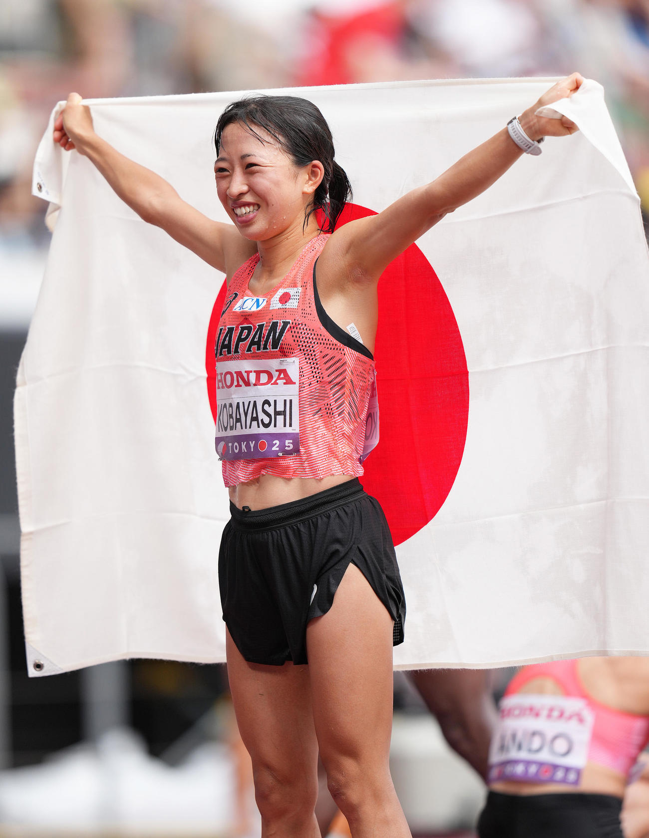 女子マラソンで7位入賞を果たし日の丸を手に笑顔を見せる小林（撮影・足立雅史）