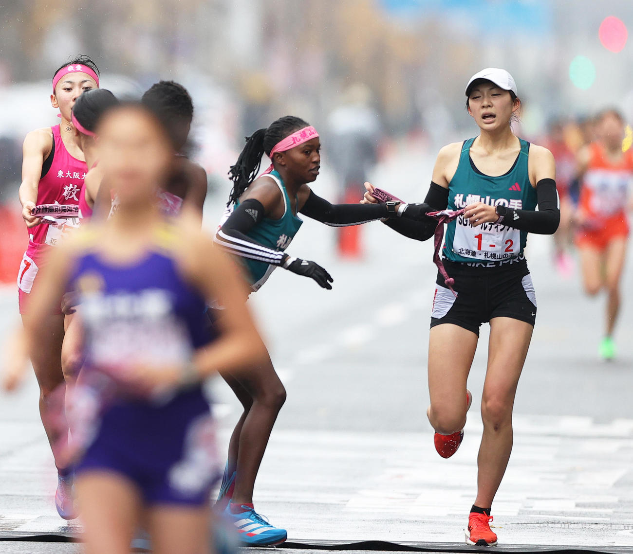 札幌山の手2区の長谷川（右）は第2中継所で3区のニャンブラにタスキをつなぐ（撮影・上山淳一）