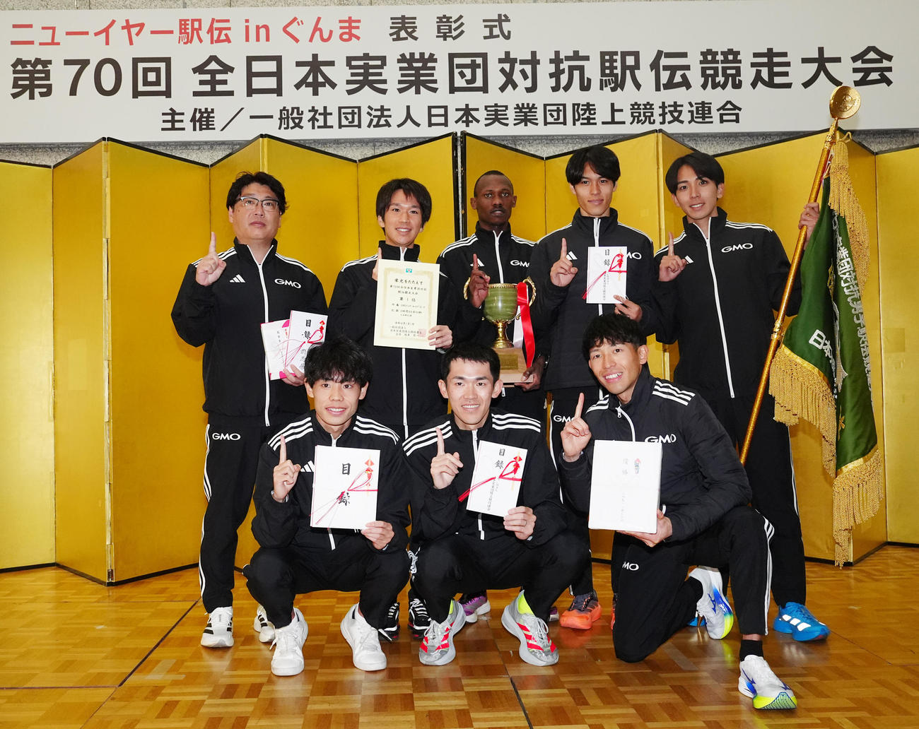 ニューイヤー駅伝で優勝し表彰式で写真に納まるGMOインターネットグループの選手たち。前列左から2区今江、3区鈴木、6区嶋津、後列左から伊藤監督、1区吉田、4区テモイ、5区太田、7区鶴川（撮影・江口和貴）