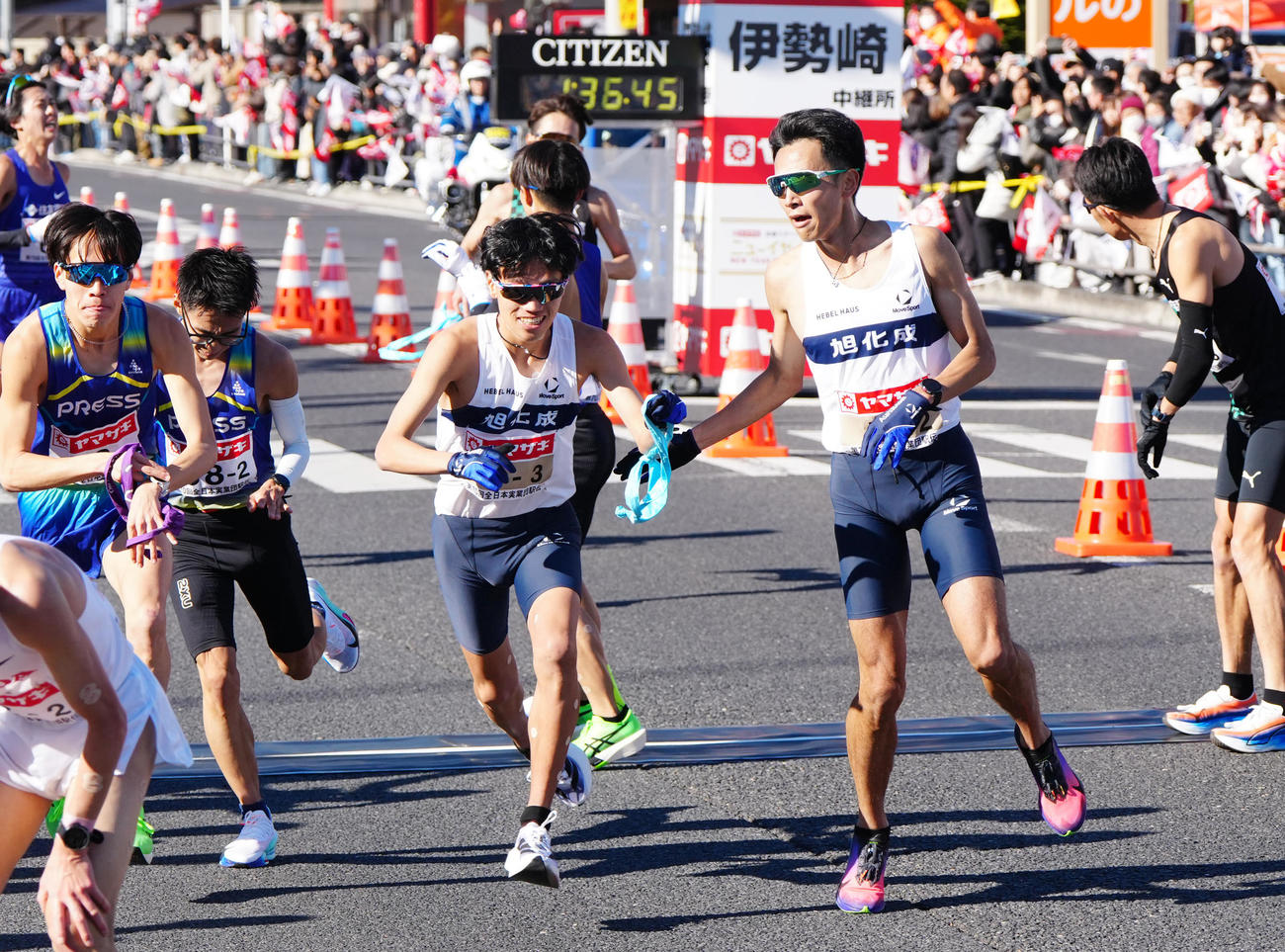 ニューイヤー駅伝の第2中継所でタスキリレーする旭化成2区相沢（中央右）と3区山本（撮影・江口和貴）