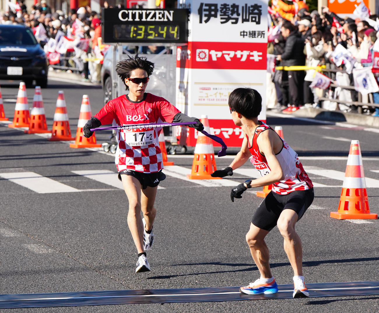 ニューイヤー駅伝の第2中継所でサンベルクス3区越（右）にタスキを渡す2区吉田（撮影・江口和貴）