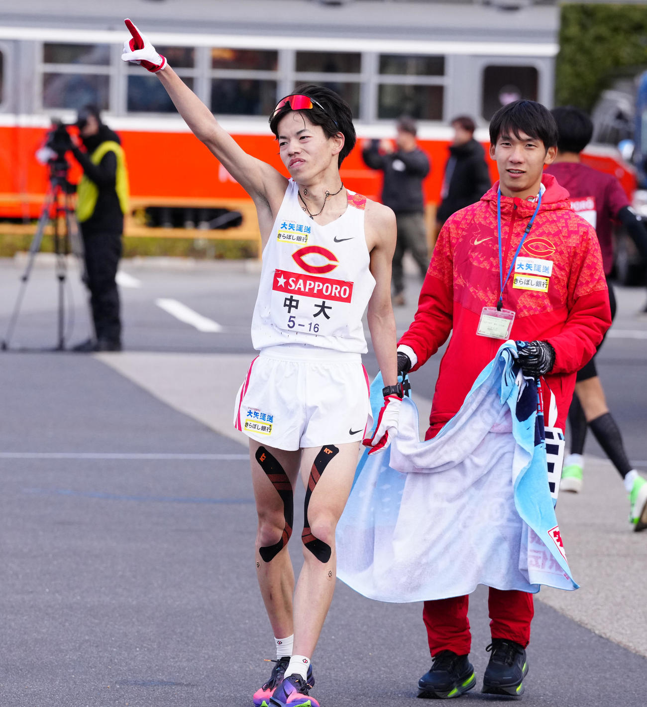 小田原中継所1位でたすきを渡し、指を突き上げる中大4区岡田（左）（撮影・鈴木みどり）