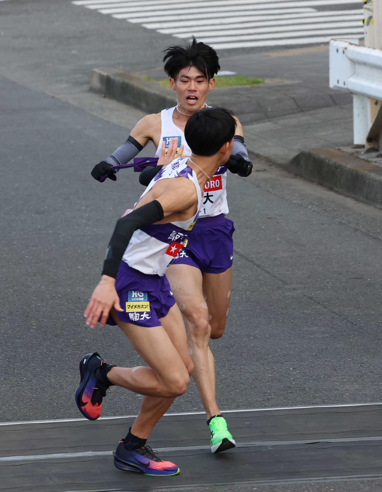 鶴見中継所で駒大・桑田（手前）にタスキリレーをする小山（撮影・増田悦実）