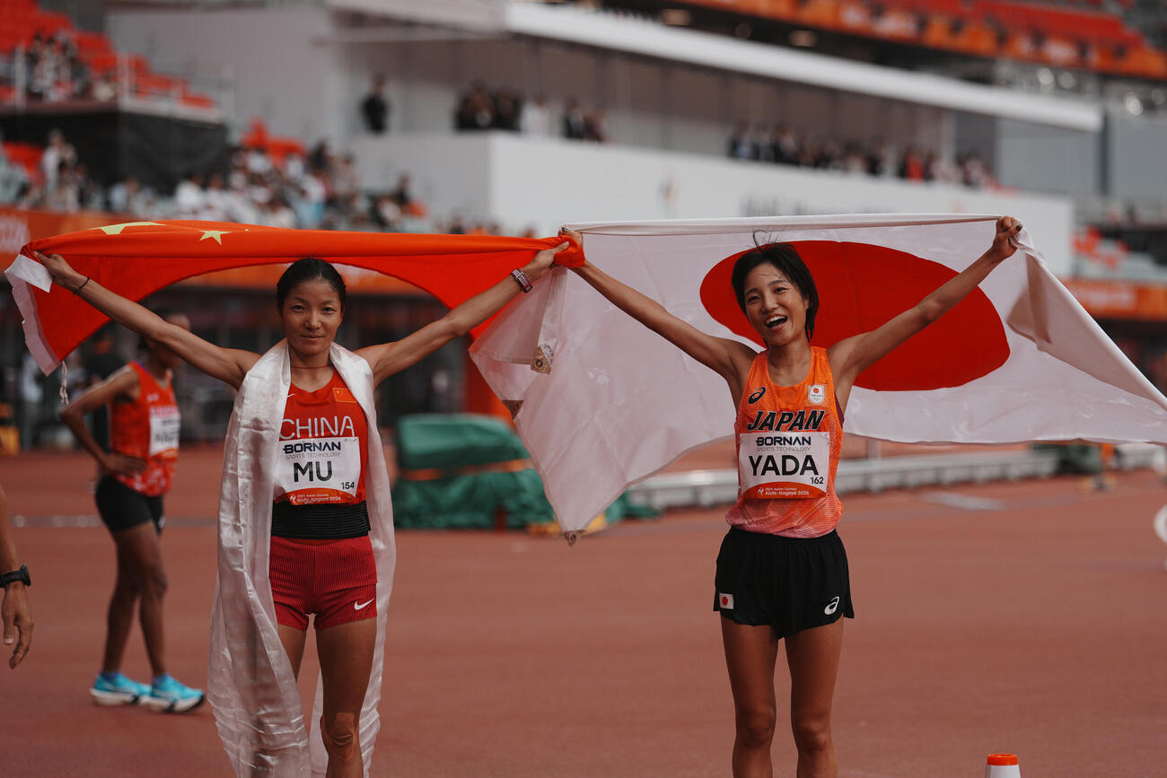 アジア大会女子マラソンで銅メダルを獲得した矢田みくに（右）と銀の中国・次仁措姆は互いの国旗を広げて記念撮影する（AP）