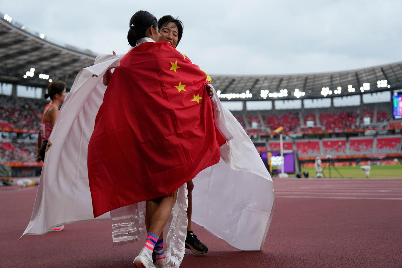 アジア大会女子マラソンで銅メダルを獲得した矢田みくに（右）は、銀の中国・次仁措姆と互いの国旗をまとってハグする（AP）