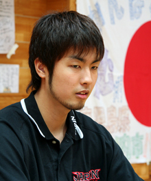 応援メッセージの書かれた日の丸の前でインタビューに答える竹内公
