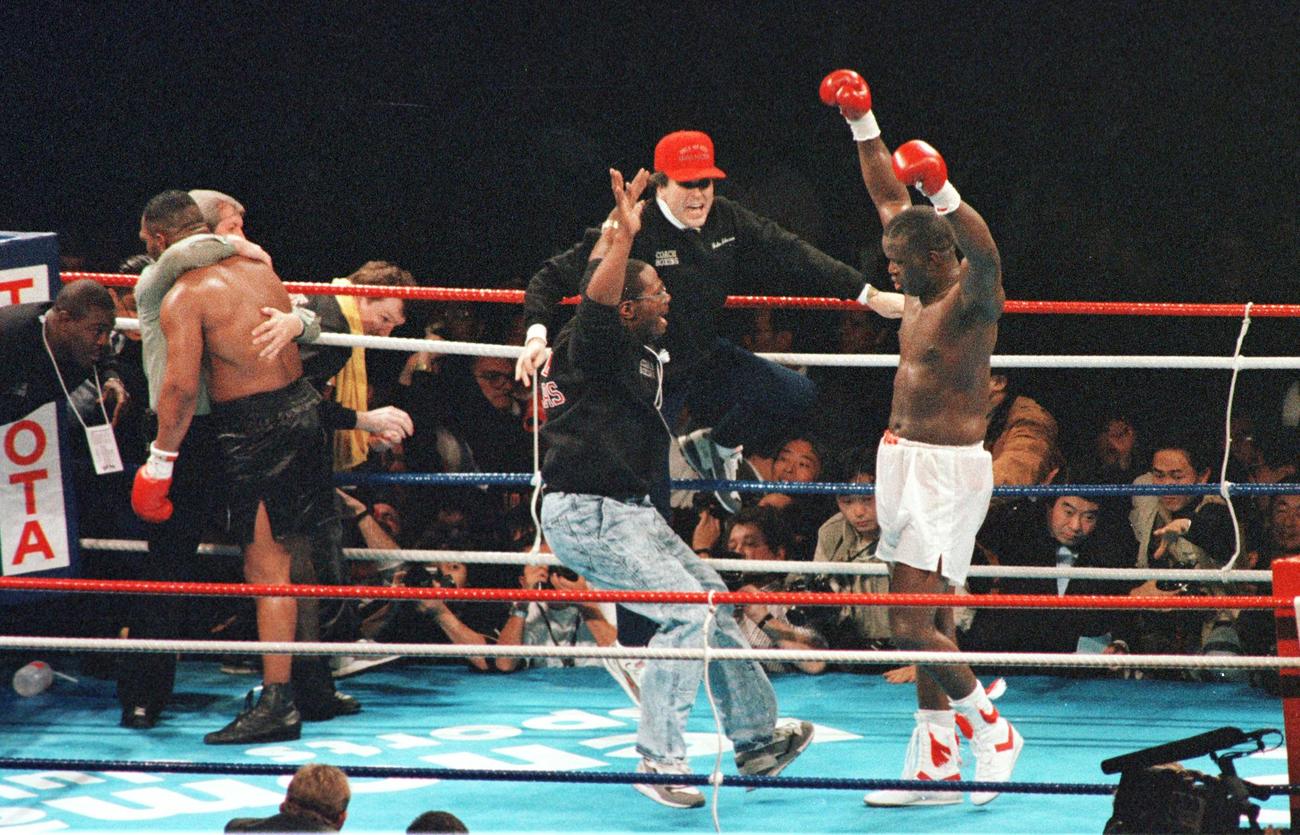 WBA・IBF・WBC世界ヘビー級タイトルマッチ　マイク・タイソン対ジェームス・ダグラス　10回、KO勝ちし両手を浮き上げ喜ぶジャームス・ダグラス（右）　左から2人目はKO負けを喫しレフェリーに抱えられるマイク・タイソン（1990年2月11日撮影）　