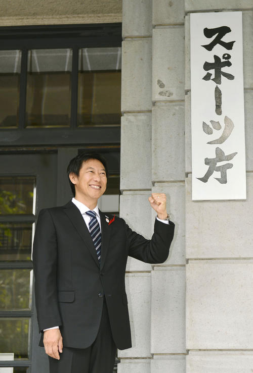 スポーツ庁が発足し、新しく掛けられた看板の前でガッツポーズする鈴木大地初代長官