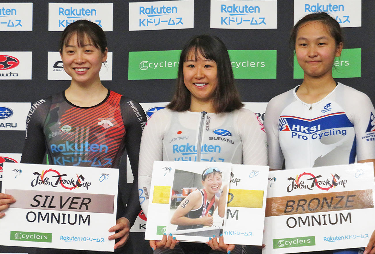 女子オムニアムを優勝した梶原悠未（中央）は、事故で亡くなった親友宮崎集さんの写真を手に表彰台に上がる