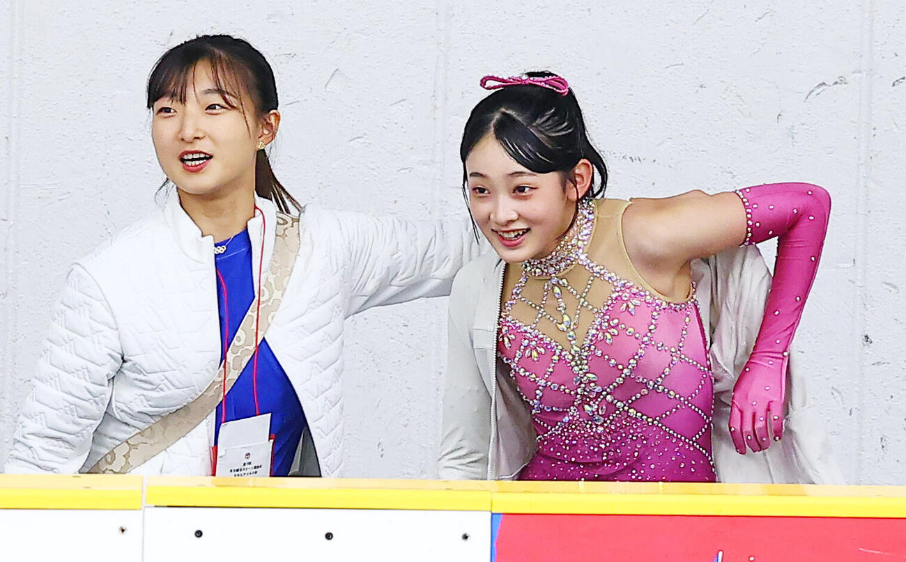 リンクサイドで亀井美杜（右）にウェアを着せる神戸クラブの坂本花織コーチ（撮影・野上伸悟）
