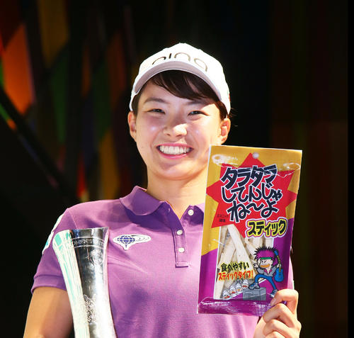 渋野はトロフィーとプレー中に食べていた菓子「タラタラしてんじゃね～よ」を手に笑顔を見せる（撮影・足立雅史）