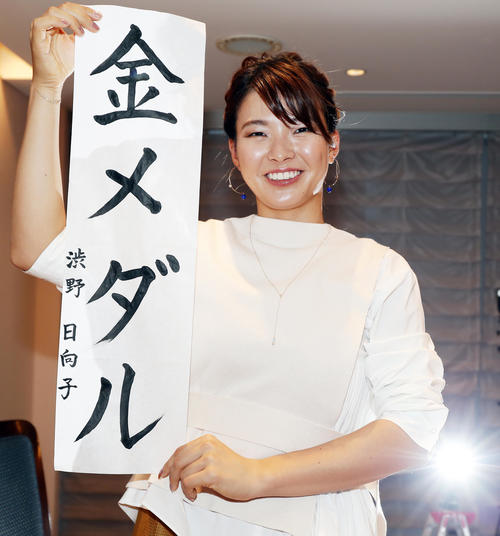 「金メダル」と毛筆で書いた書を手に笑顔を見せる渋野（撮影・浅見桂子）