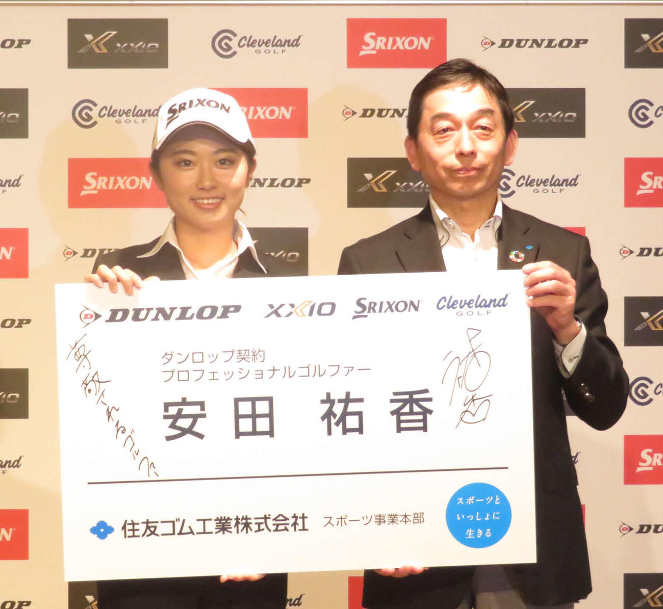 「尊敬されるゴルファー」と目標を記した巨大名刺を手に笑顔を見せる安田祐香（左）。右は住友ゴム工業の川松スポーツ事業本部長