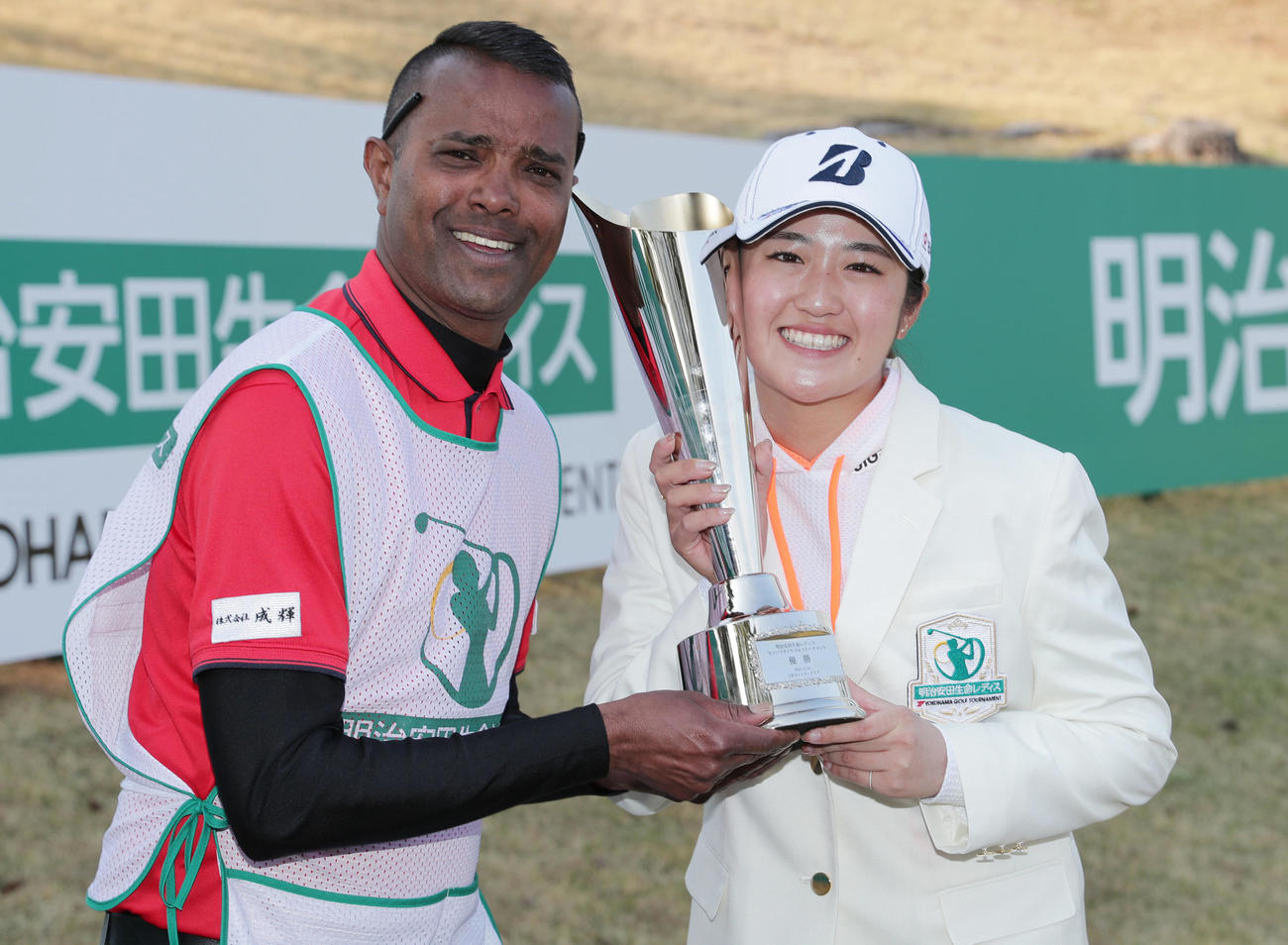 トロフィーを手に笑顔を見せる稲見萌寧（右）とキャディーのセナ・チャンドさん（撮影・前田充）