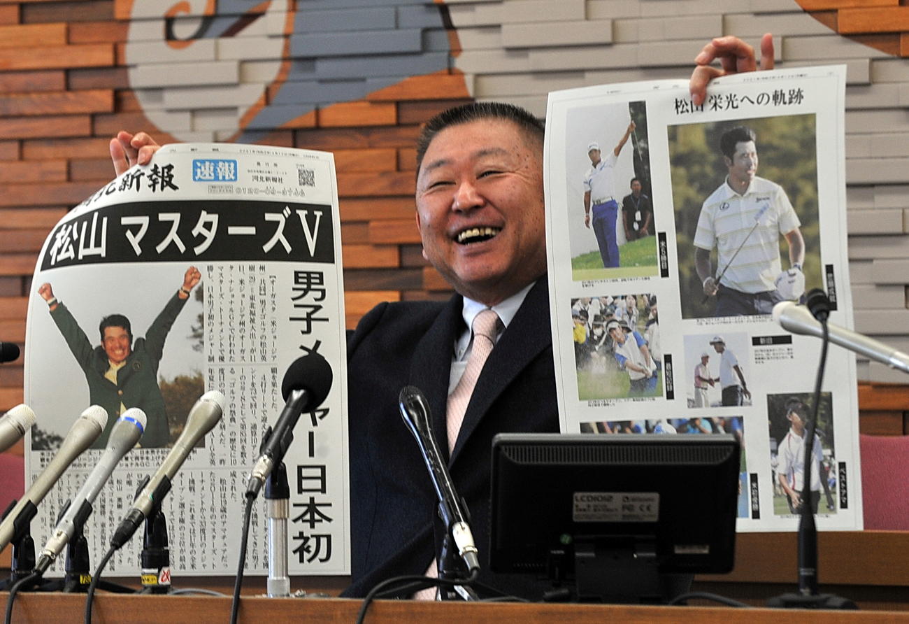東北福祉大ゴルフ部の阿部監督は会見で松山のメジャー制覇を報じる地元紙の号外を掲げて笑顔を見せる