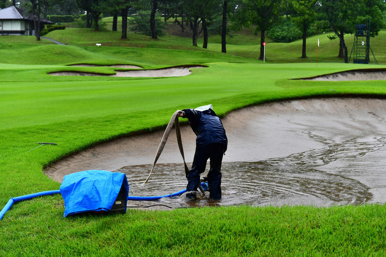 4番グリーンそばのバンカーにたまった水をポンプで抜くゴルフ場関係者。懸命な作業も及ばず2日連続で悪天候のため中止となった（21年7月2日撮影）