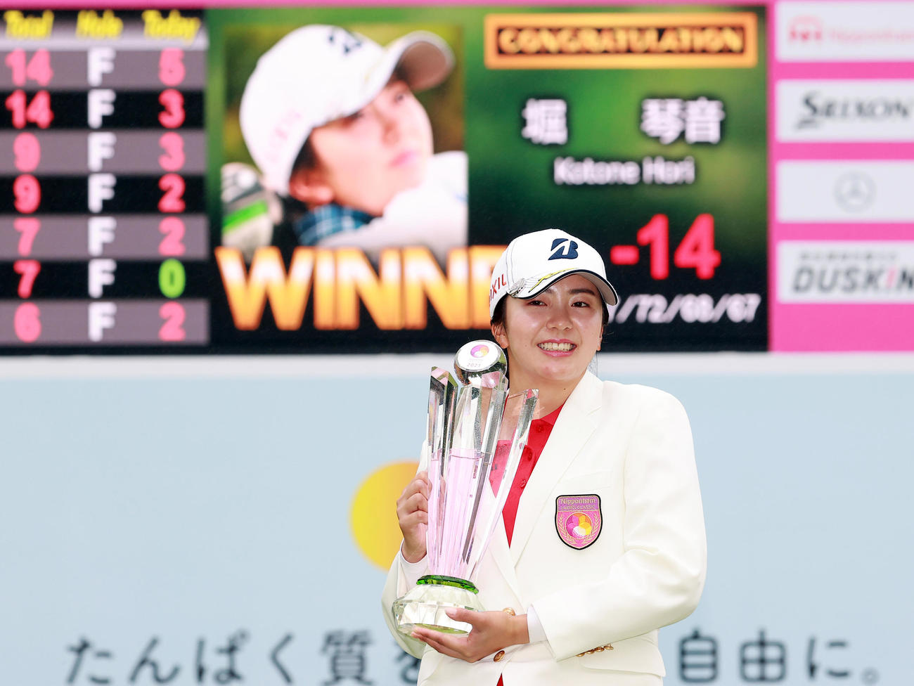 プレーオフを制して初優勝を決めた堀は、スコアボードを背にトロフィーを抱く（撮影・浅見桂子）