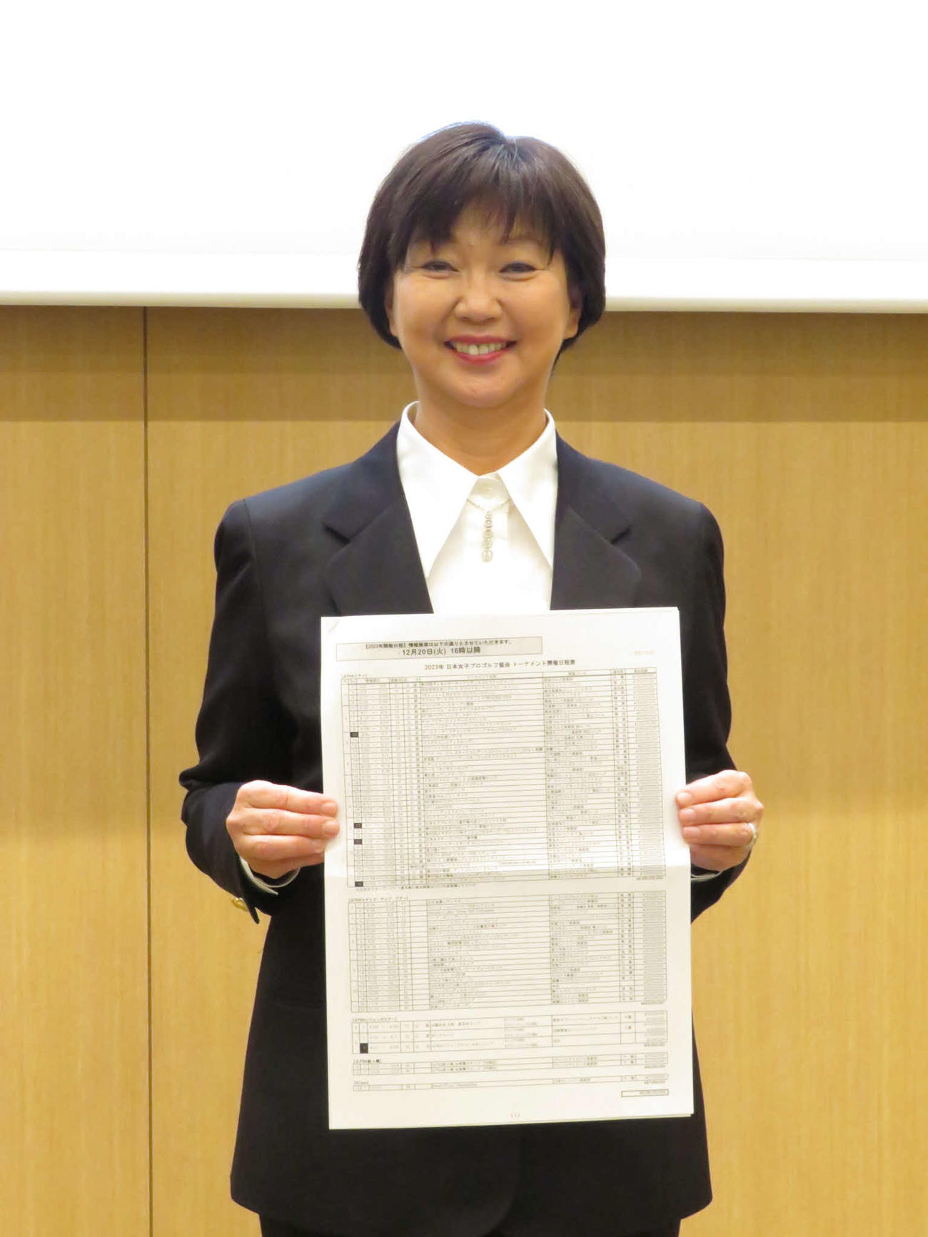 来季日程の一覧表を手に笑顔を見せるJLPGAの小林会長