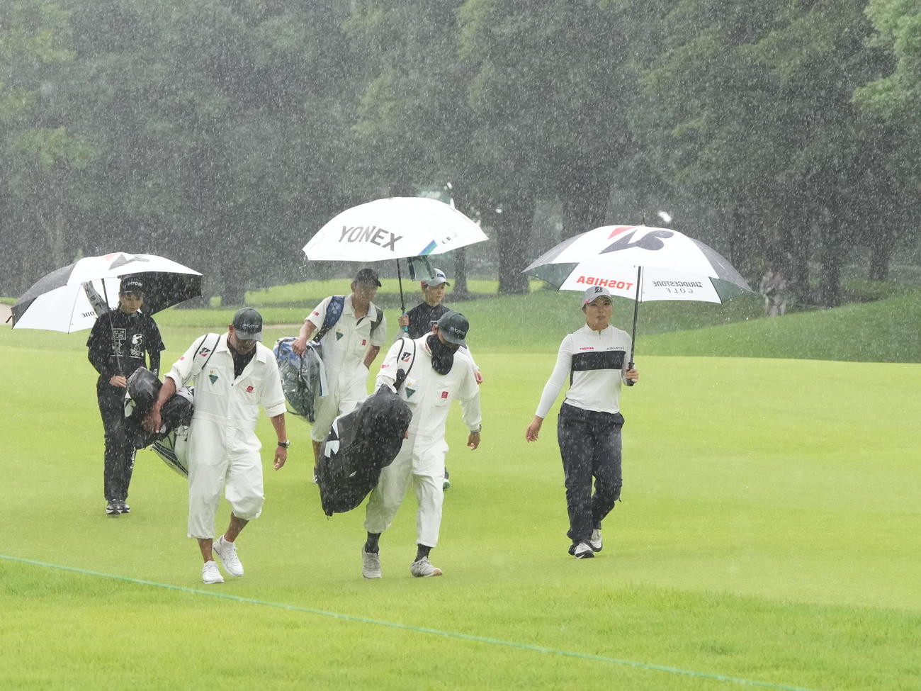 アースモンダミンカップ2日目、12番、雨のため競技が一時中断となりコースを引き揚げる高橋（右）ら選手たち（撮影・小沢裕）