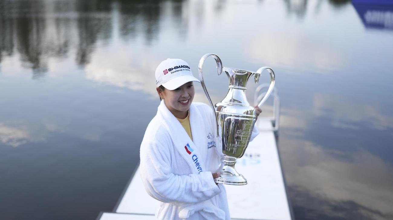 シェブロン選手権で優勝し、池へのウイニングダイブ後、チャンピオンシップ・ローブを着てトロフィーを掲げる西郷真央（AP）